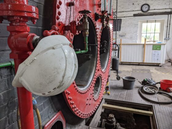 White hard hat hung on bright red pipe in front of bright red boiler